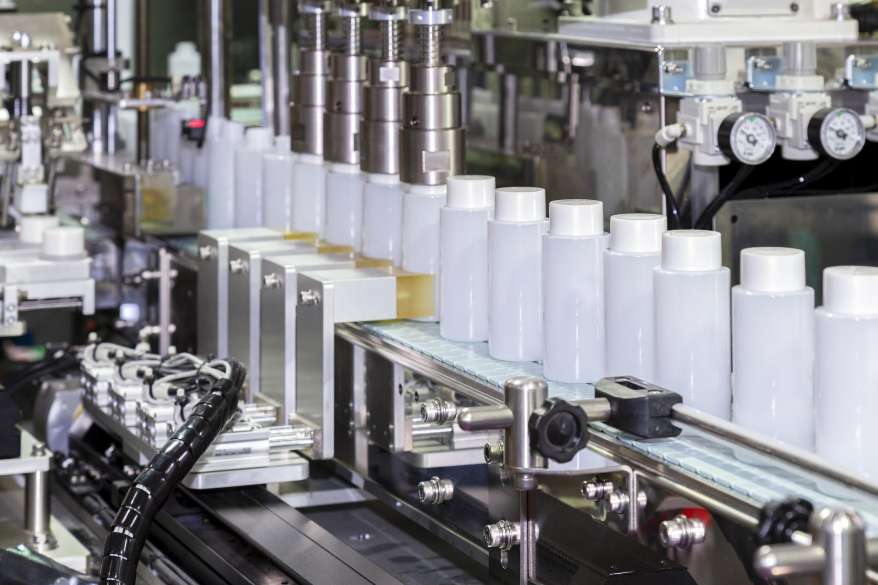 Botella de plástico blanca moviéndose sobre una cinta transportadora de una máquina etiquetadora y tapadora automática en una fábrica de cosméticos y productos para el cuidado de la piel. Concepto de maquinaria con tecnología de inteligencia artificial y para la industria cosmética.